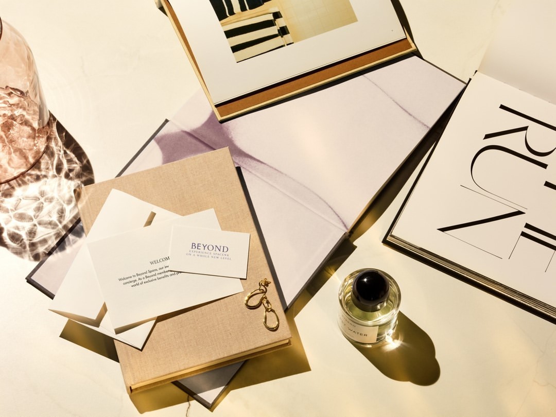 Still life with perfume bottle, magazines, books, and gold earrings on a white surface with soft, natural light creating a calm aesthetic.
