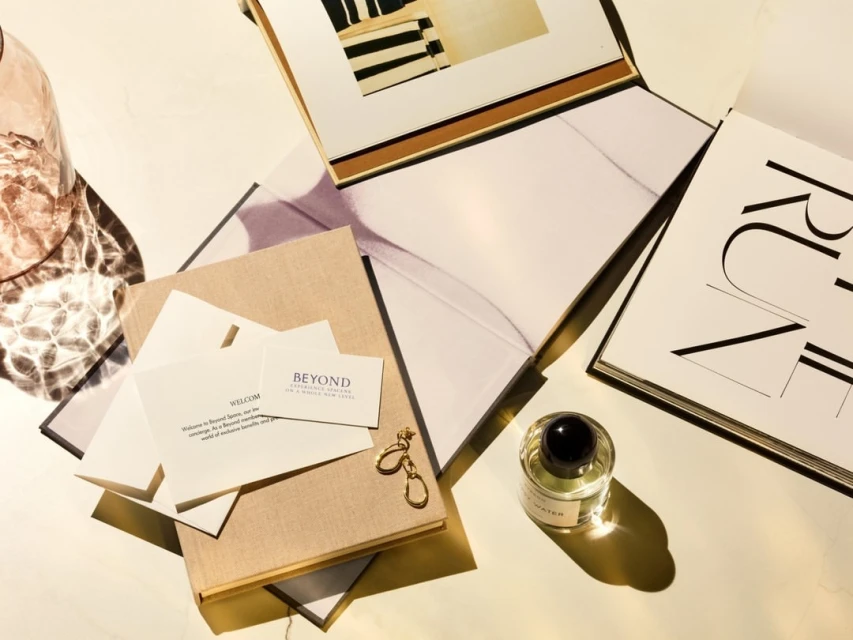 Still life with perfume bottle, magazines, books, and gold earrings on a white surface with soft, natural light creating a calm aesthetic.