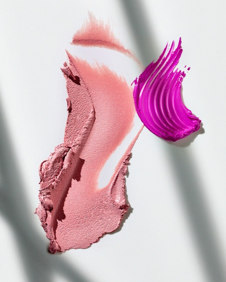 Cosmetic product smears in pink and purple hues on a white surface with soft lighting and shadows. Beauty and makeup still life.