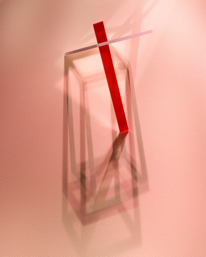 Abstract geometric composition featuring a red stick, transparent plane, and a rectangular frame against a peach-toned backdrop.