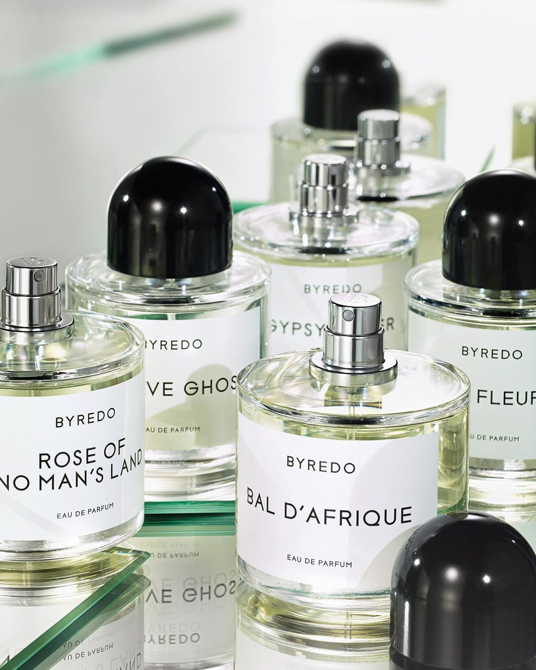 Close-up of Byredo perfume bottles with various fragrances on a reflective surface, showcasing minimalist design and sleek packaging.