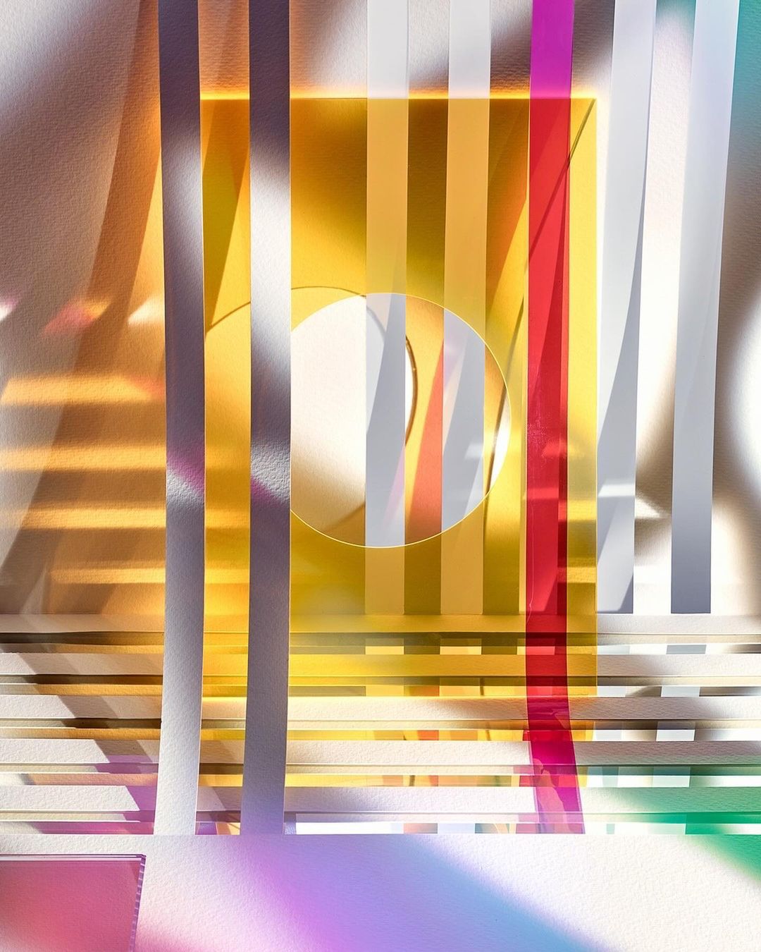 Abstract still life featuring vertical translucent colored glass or plastic strips, a central white circle, and rainbow gradient lighting.