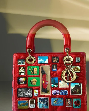 Close-up of a red Lady Dior handbag with a short top handle and various small, square images and charms attached, showcasing luxury fashion.