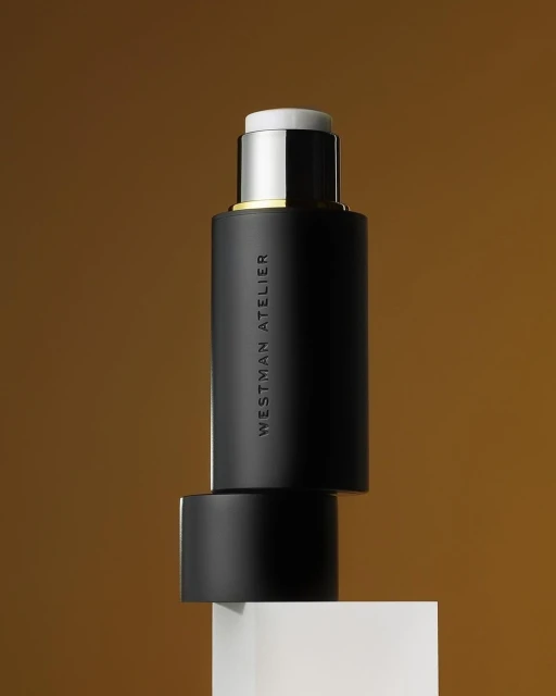 Elegant product shot of Westman Atelier makeup stick against a gradient brown backdrop, resting on a small white cube.