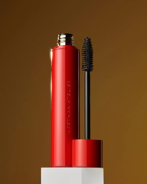 Still life studio shot of red Westman Atelier mascara tube with black wand, against a golden gradient background on a white block.