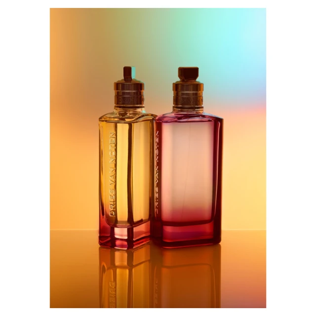 Two bottles of Dries Van Noten perfume stand on a reflective surface, with gradient hues of yellow, orange, red, and blue in the background.