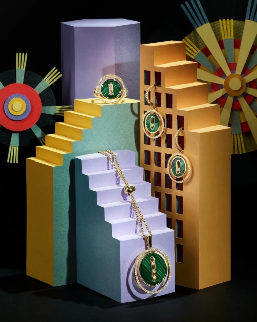 Elevated jewelry arrangement featuring a gold chain necklace, earrings, and ring with green malachite stones set atop geometric steps.