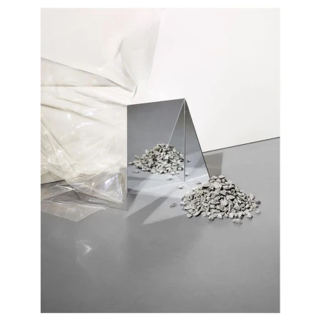 Abstract still life featuring scattered grey rocks near a reflective triangular mirror, set against white and grey surfaces.