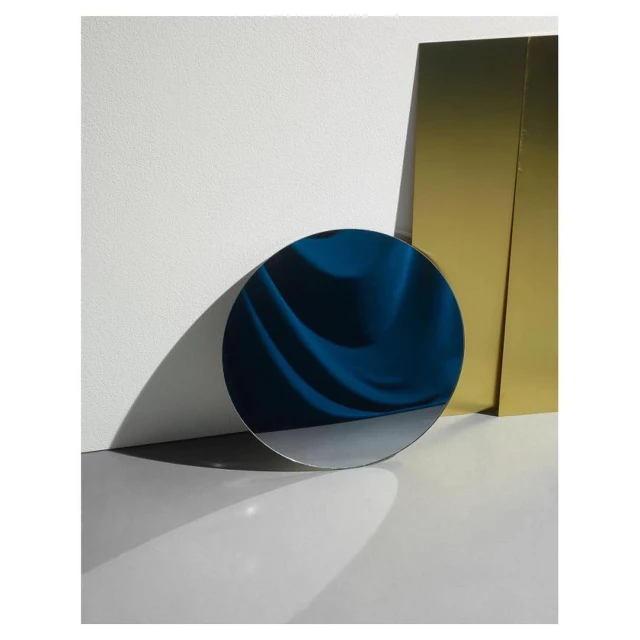 Abstract composition with a blue circular form in the foreground, a gold rectangular form, and a white wall in the background.