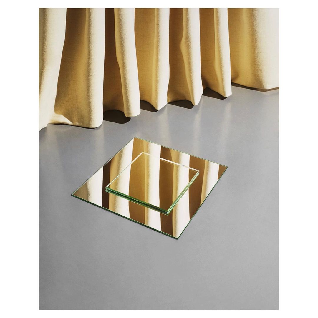 Still life of two square glass mirrors on a gray surface, reflecting draped yellow fabric, casting soft shadows in a minimalist composition.