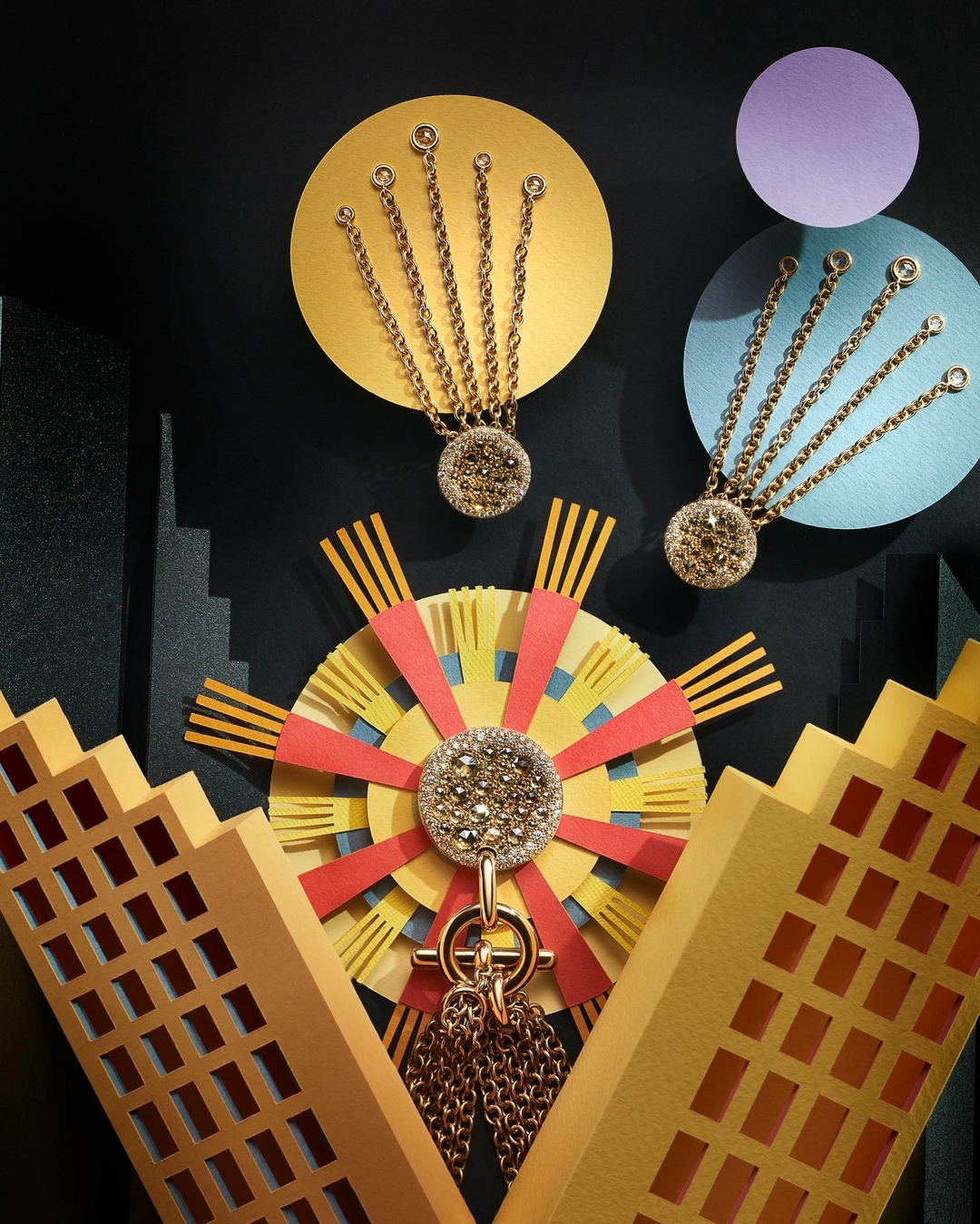 Conceptual jewelry still life featuring gold pendants with gemstone accents, against a black background with yellow, red, and blue paper shapes.