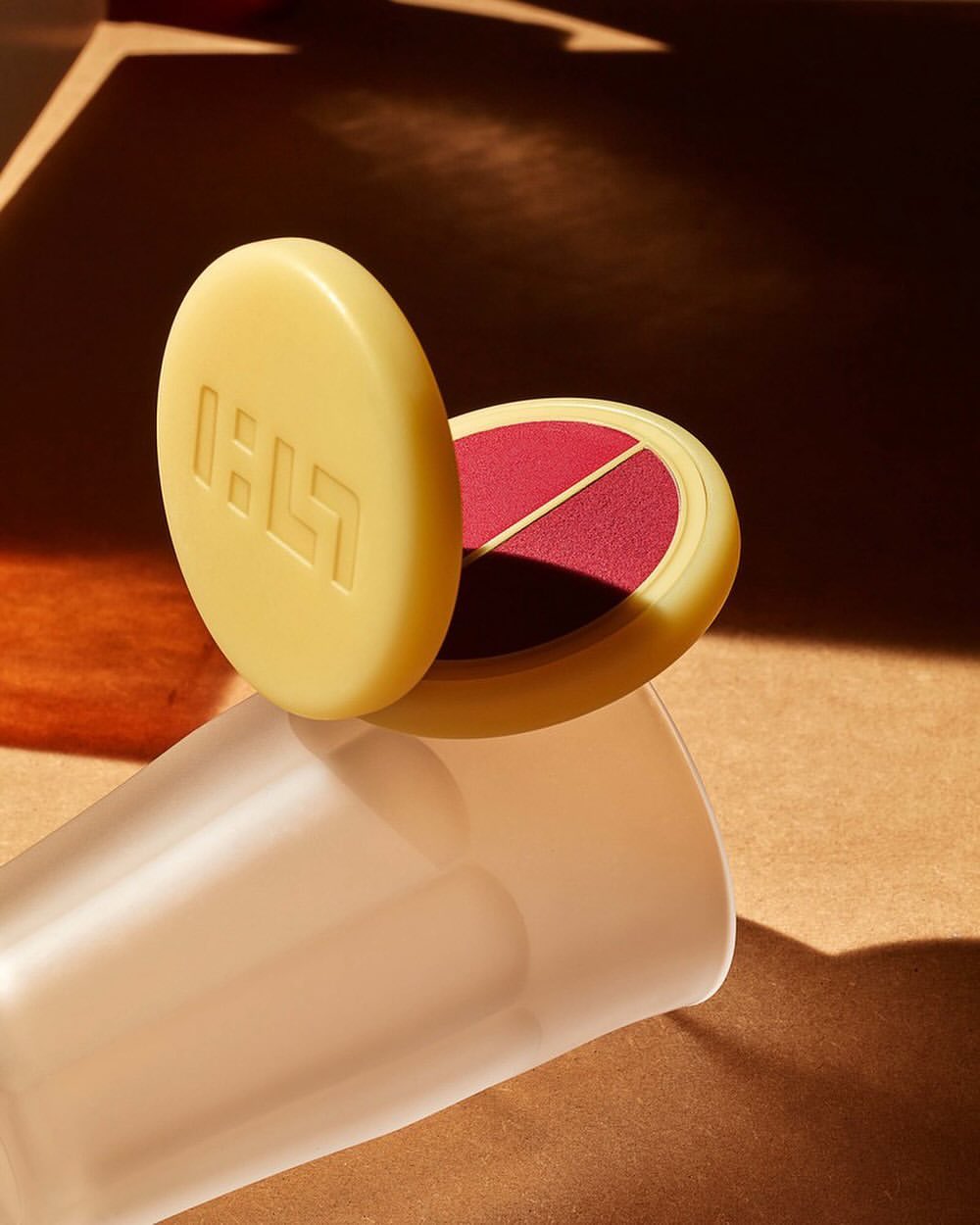 Beige makeup compact with blush on warm brown surface with graphic shadows and frosted glass - beauty and cosmetics product shot.