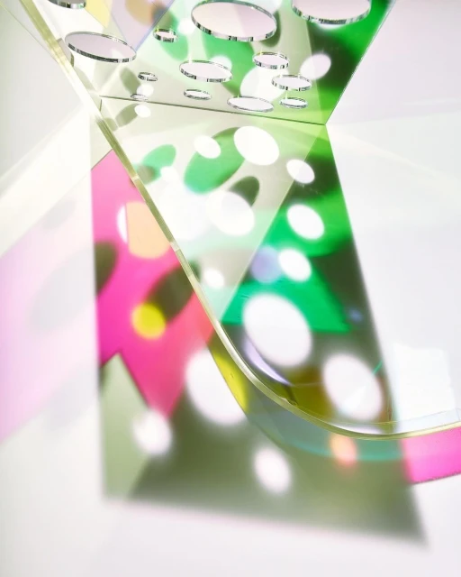 Abstract still life of curved transparent acrylic sheets casting colorful shadows with polka dots on a white surface in bright studio light.