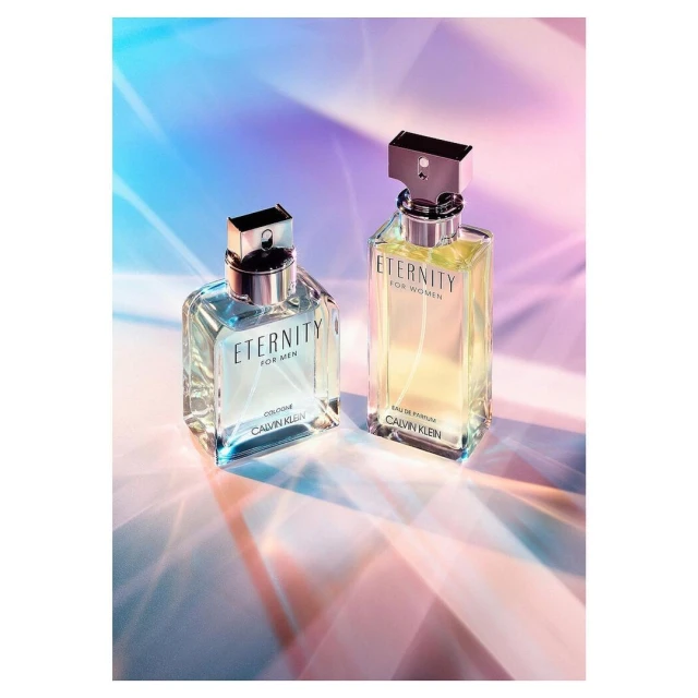 Two Calvin Klein Eternity perfume bottles, for men and women, arranged on a surface reflecting a colourful light pattern.