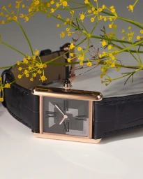 Cartier watch with black leather strap on a white background adorned with yellow wildflowers