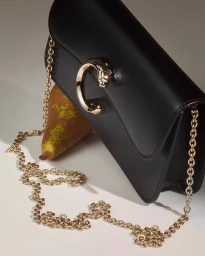 Black leather shoulder bag with gold chain strap resting against a ripe pear on white seamless backdrop