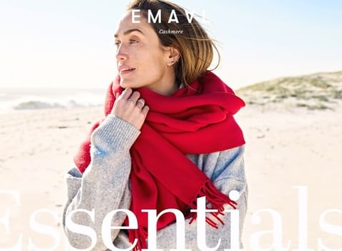 Woman wearing a grey knit sweater and a large red scarf outdoors on a sandy beach by the ocean