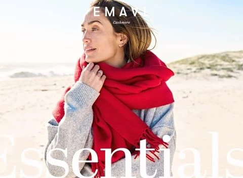 Woman wearing a grey knit sweater and a large red scarf outdoors on a sandy beach by the ocean