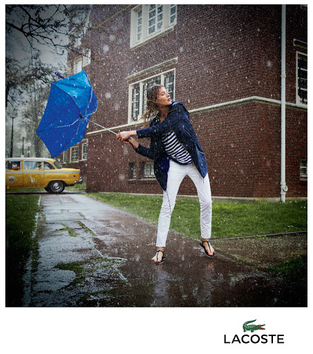 Woman holding a blue inverted umbrella in heavy rain wearing a blue jacket and white trousers with a yellow car in the background.