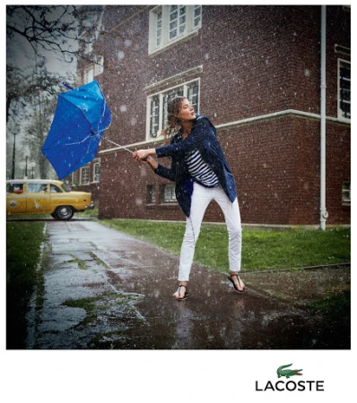 Woman holding a blue inverted umbrella in heavy rain wearing a blue jacket and white trousers with a yellow car in the background.