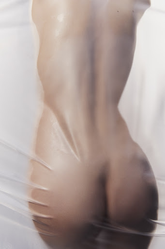 Back view of a nude adult female figure covered in clear plastic, showcasing form and texture against a white background.