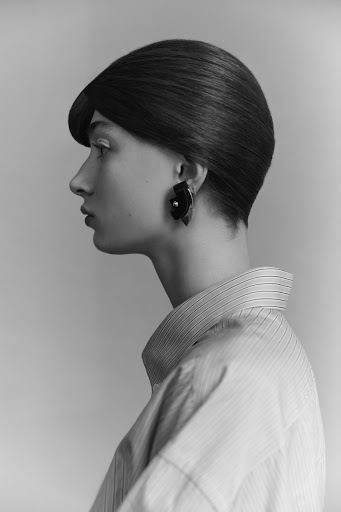 Monochrome portrait of a stylish adult woman in a striped shirt and modern earrings posing in a photo studio setting.