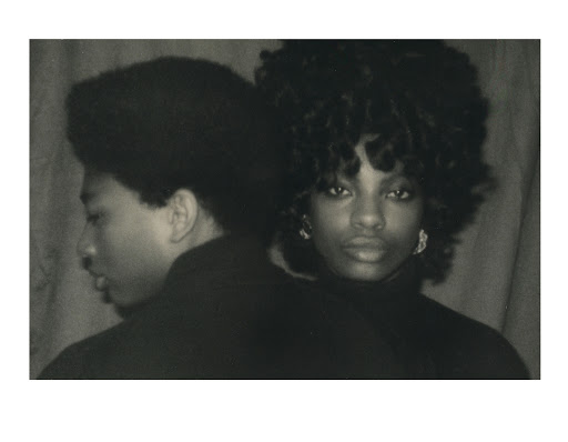 Monochrome portrait of an African-American man and woman with dark curly hair, dressed in dark clothing in a simple indoor setting.