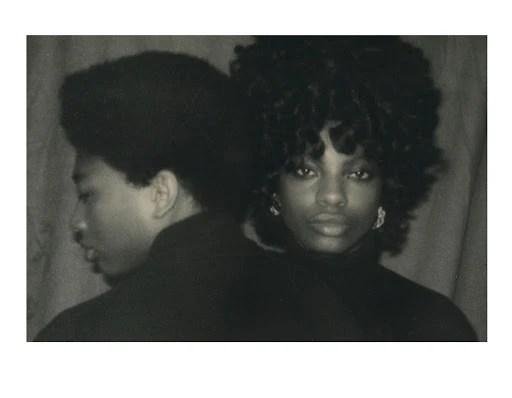 Monochrome portrait of an African-American man and woman with dark curly hair, dressed in dark clothing in a simple indoor setting.