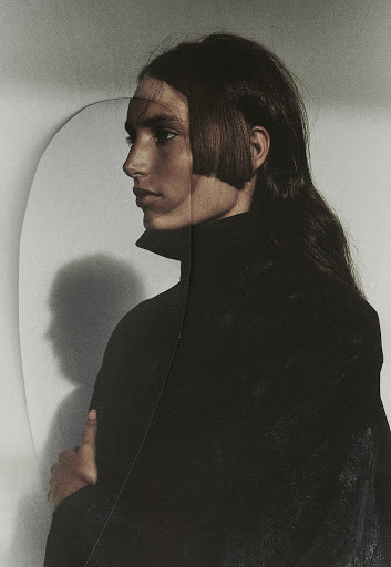 Portrait of an adult woman with a bob hairstyle and long dark hair, wearing a black jacket in a white-walled indoor studio setting.