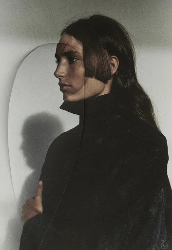 Portrait of an adult woman with a bob hairstyle and long dark hair, wearing a black jacket in a white-walled indoor studio setting.