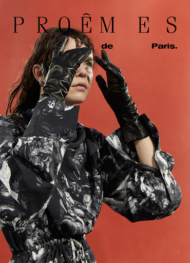 Fashion shot of a woman in a patterned dress and black gloves, posing with her hands up against a terracotta background with text.