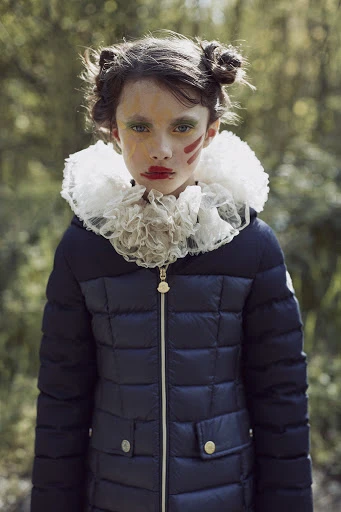 Portrait of a young girl with theatrical makeup posing in a puffy jacket with a large ruffled collar in an outdoor setting.