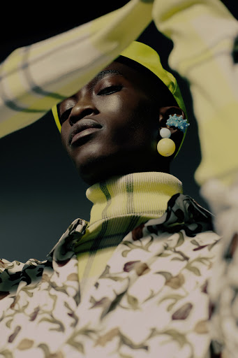Fashion portrait of a stylish adult with green beret and floral jacket against a dark backdrop, showcasing unique earrings.