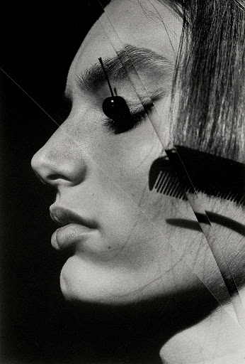 Monochrome profile portrait of a woman with a cherry resting on her eyelid and a comb cutting across her hair.