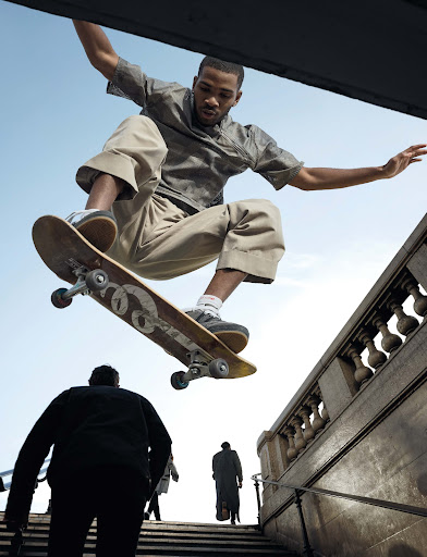 A skateboarder jumps over a set of outdoor concrete stairs with carved balustrades against an overcast sky.