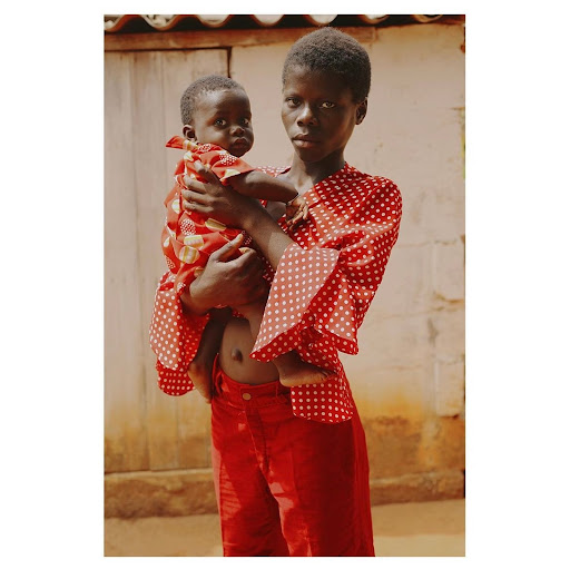 An adult woman holding a baby outside, both dressed in red and white polka dot patterned outfits, in an eye-level, medium shot.