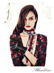 Close-up portrait of a woman wearing a floral dress, patterned scarf, and black leather gloves against a white background