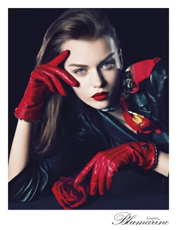 Close-up portrait of a woman wearing red leather gloves, a black leather jacket, and red lipstick, touching a red rose.