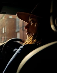 Profile of a woman wearing a wide-brimmed hat while driving a car at sunset, photographed by Beetle Rhind in London.
