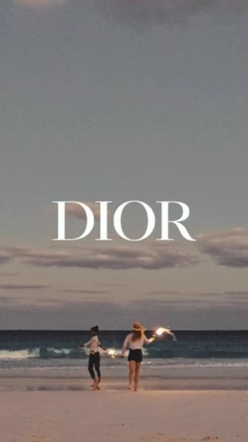 Two women walk along a beach at dusk towards the ocean. The scene is softly lit with the name 'DIOR' superimposed.