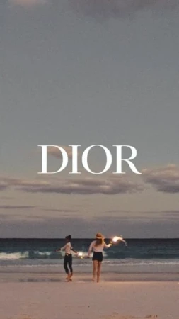 Two women walk along a beach at dusk towards the ocean. The scene is softly lit with the name 'DIOR' superimposed.