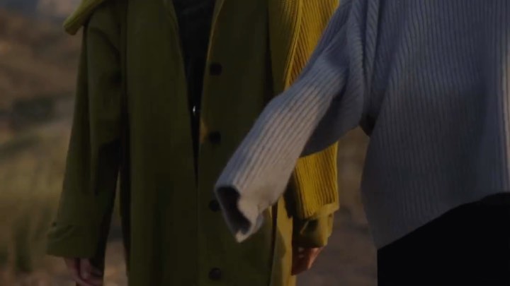 Two people in fashionable coats stand together outdoors, showcasing modern outerwear in neutral tones, creating a stylish, muted scene.