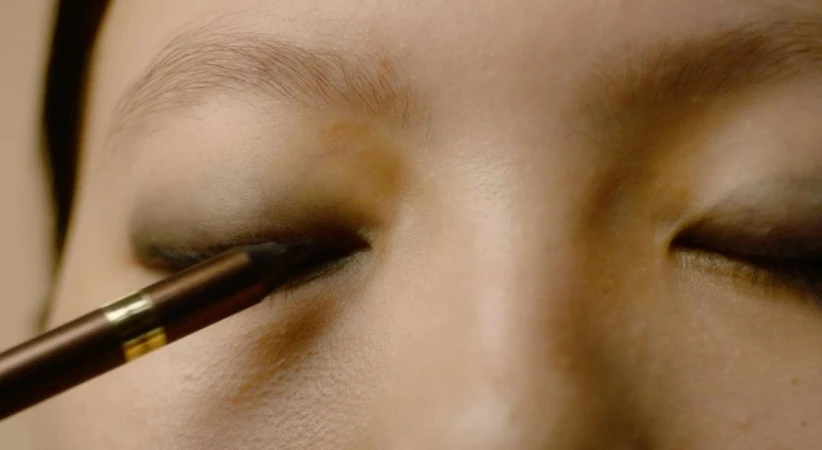 Close-up of a person applying dark eye shadow with a makeup brush, emphasizing beauty and cosmetic details on the eyelid and eyebrow.