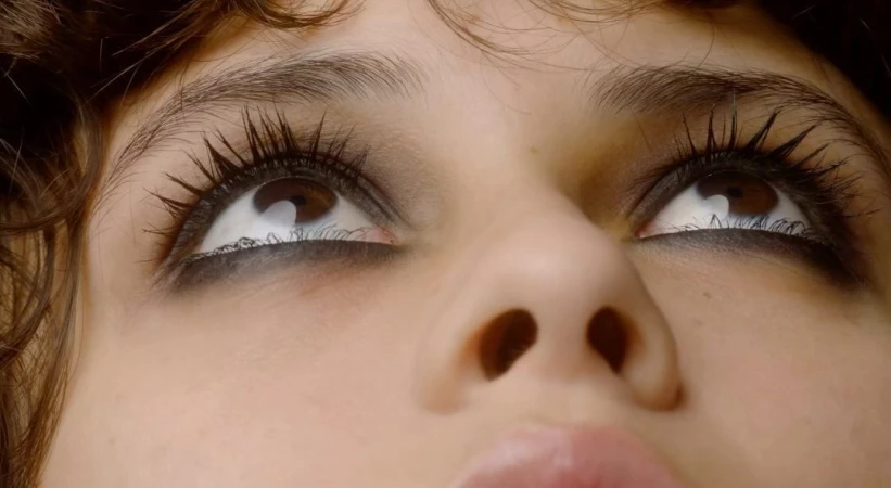 Extreme close-up portrait of a young woman looking upward with dark winged eyeliner and defined lashes captured by Belle Smith.