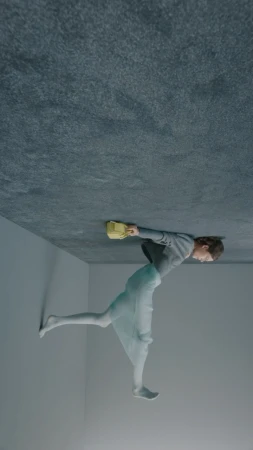 Conceptual fashion shot of a young adult female in a grey top and sheer skirt, holding a yellow purse in a grey indoor setting.