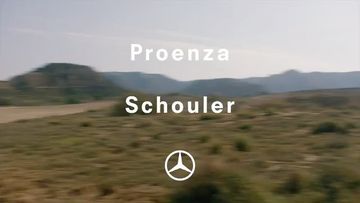 Proenza Schouler logo over a wide outdoor landscape featuring a grassy field with distant mountains under an overcast sky.