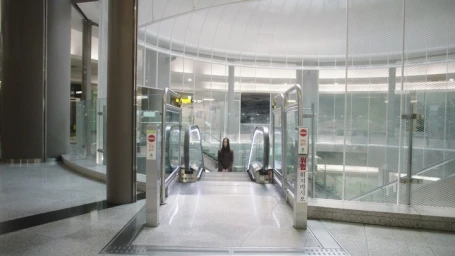 A person standing at the bottom of a halted escalator inside a modern commercial building with glass walls and metal railings.