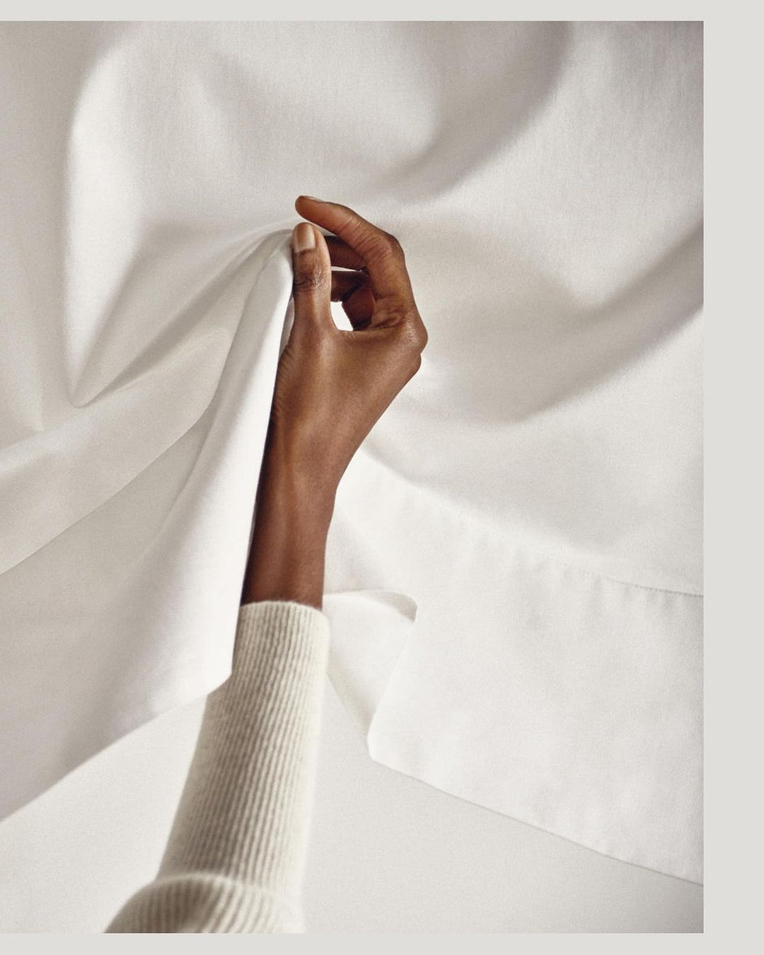 An arm and hand holding a piece of white fabric, showing material texture and a light color palette.