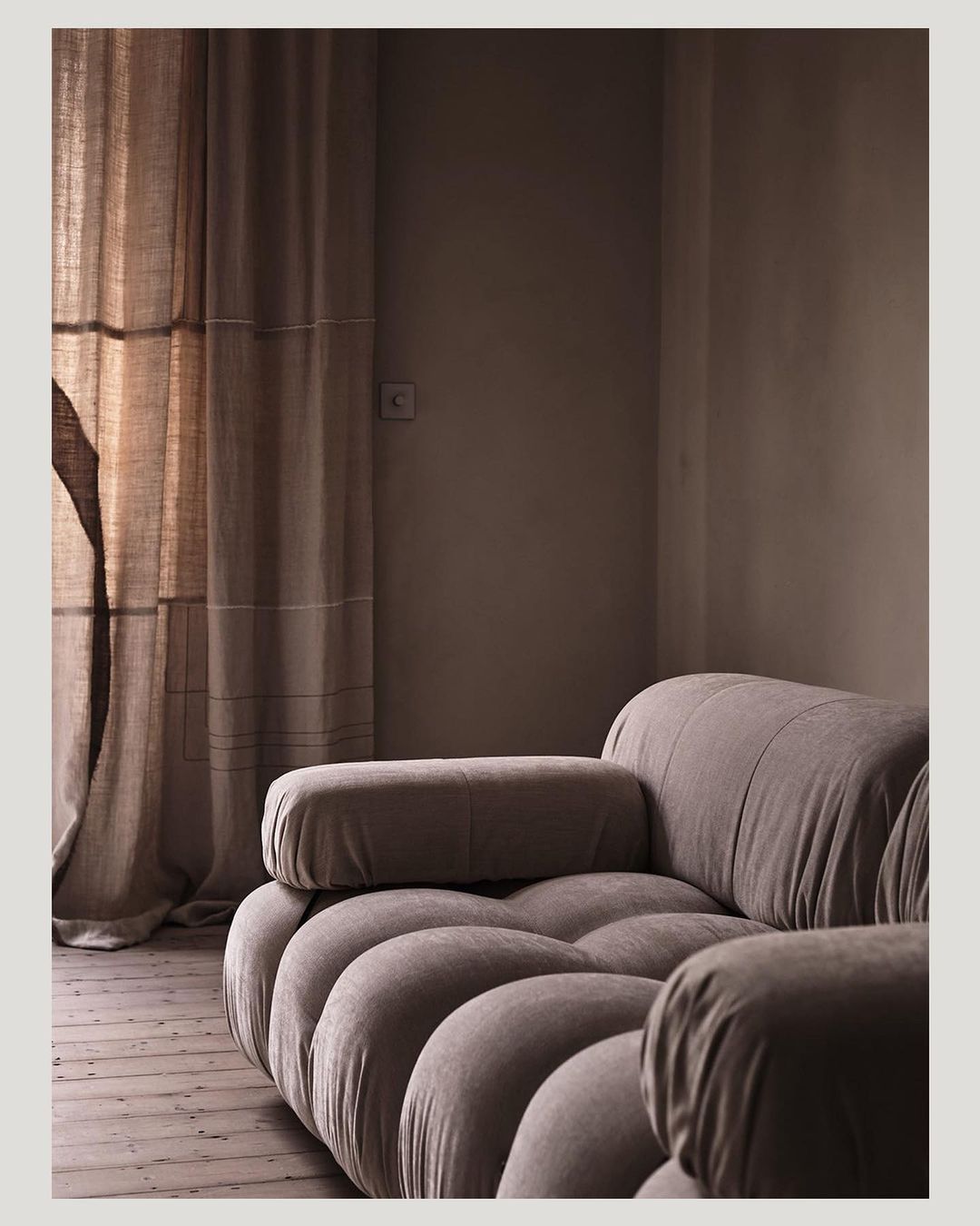 Interior shot of a neutral-toned living room featuring a modular sofa, soft lighting, and textured curtains in a home interior setting.
