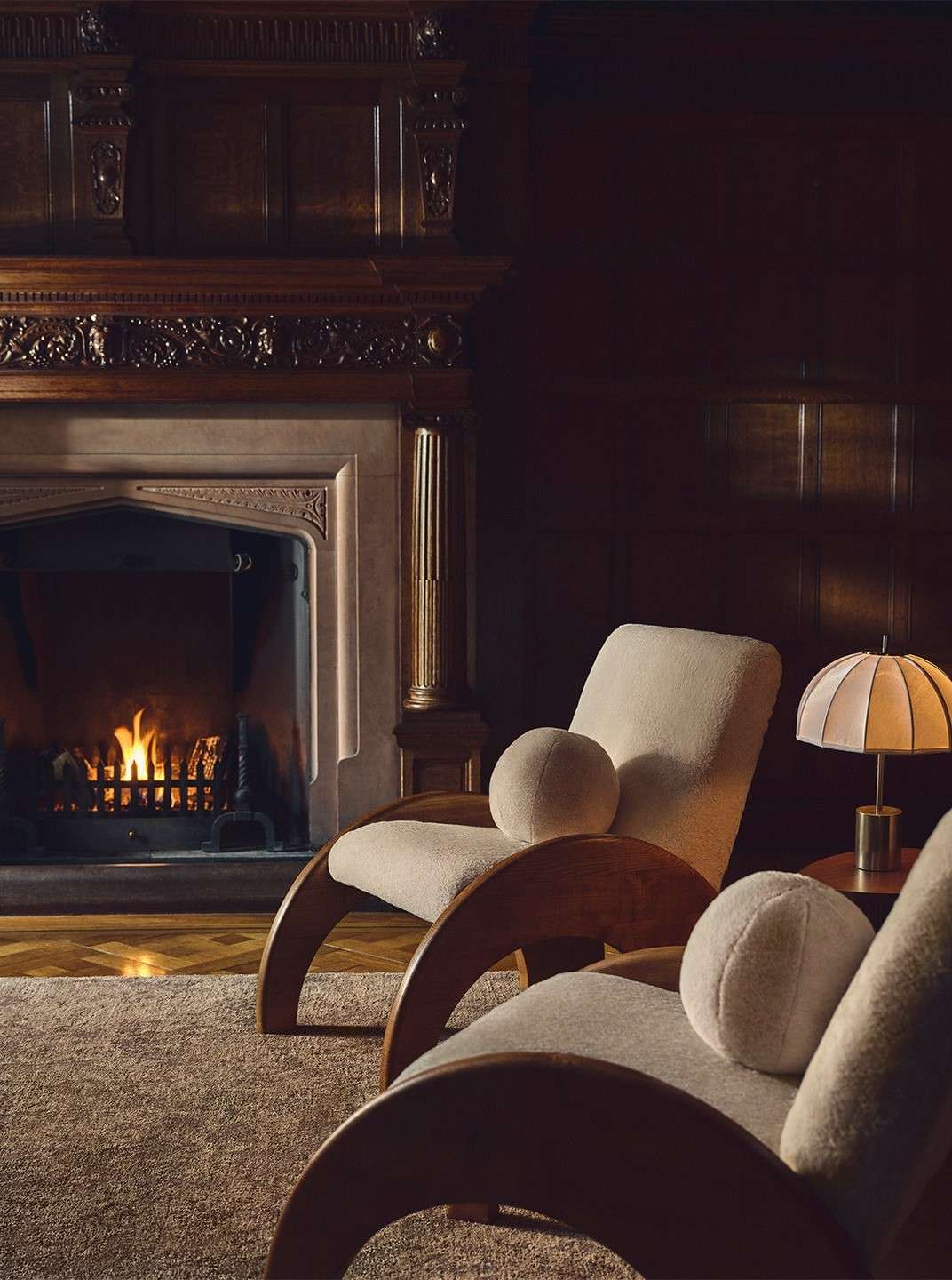 Interior design showcasing two modern armchairs with round cushions near a fireplace, set against dark wood paneling and cozy lighting.